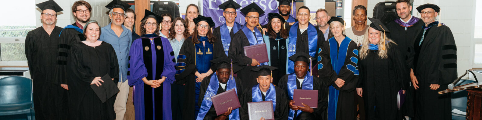 Group of graduates and faculty posing for a photo; graduates are holding up their degree covers