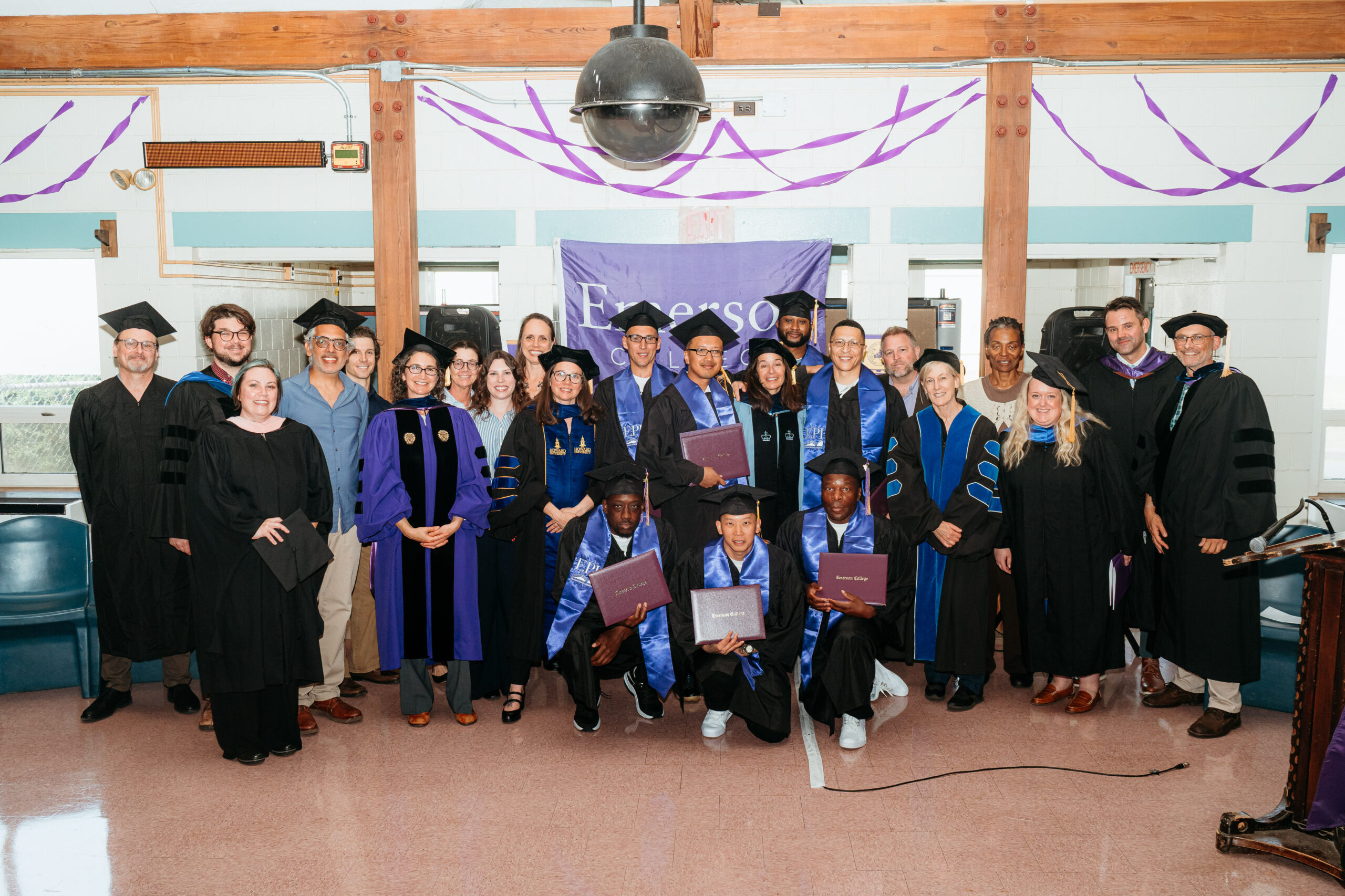 Group of graduates and faculty posing for a photo; graduates are holding up their degree covers