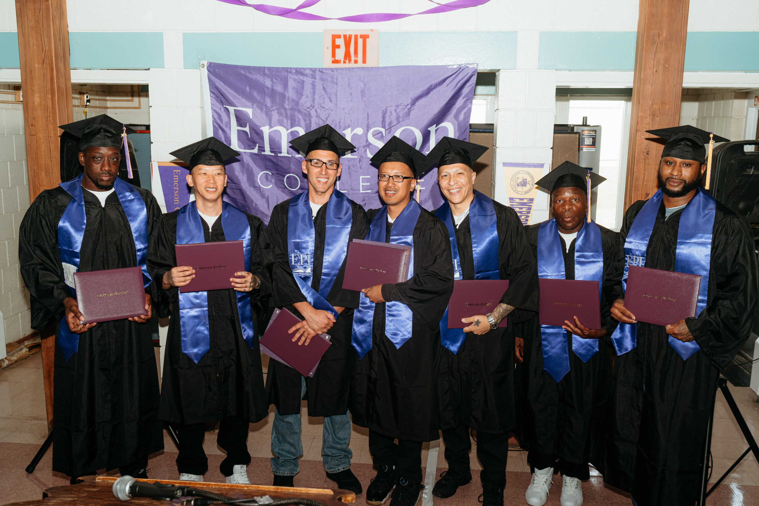 The graduating EPI cohort smiling for a photo while holding their degree covers
